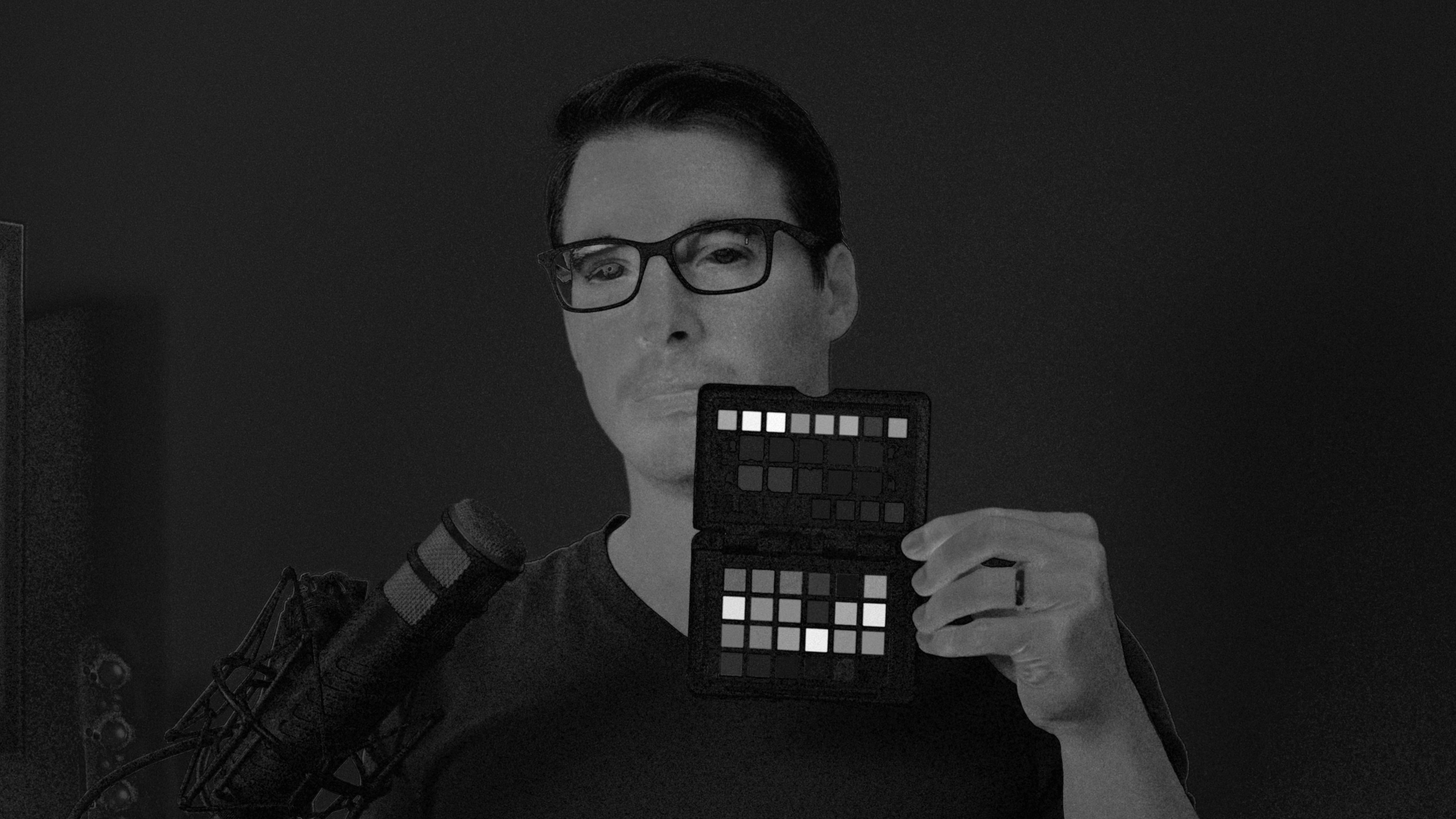 Man holding up a color checker shown in black and white depicting saturation values in the image